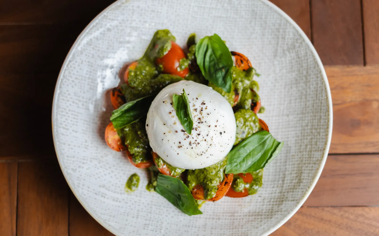 Creamy burrata with fire-roasted tomatoes and basil pesto at Noah Cape Town
